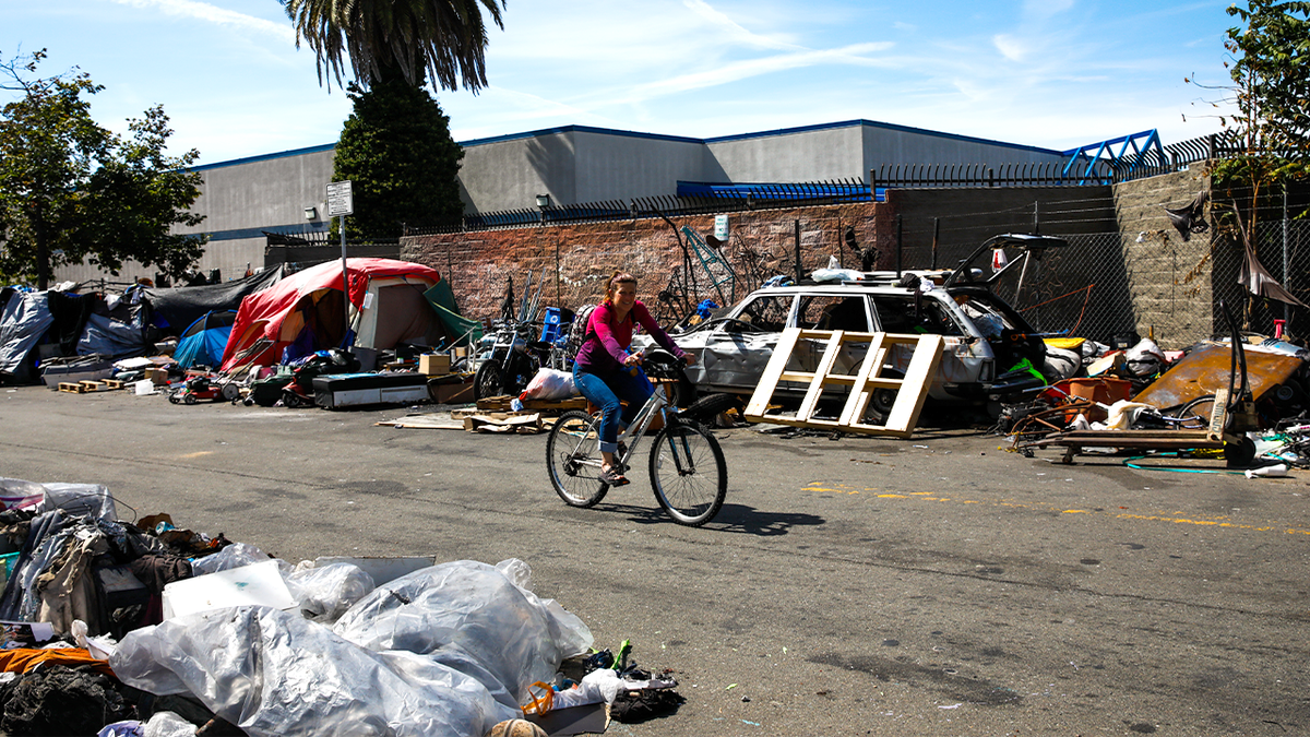 Cyclist rides past homeless encampment in Berkeley.