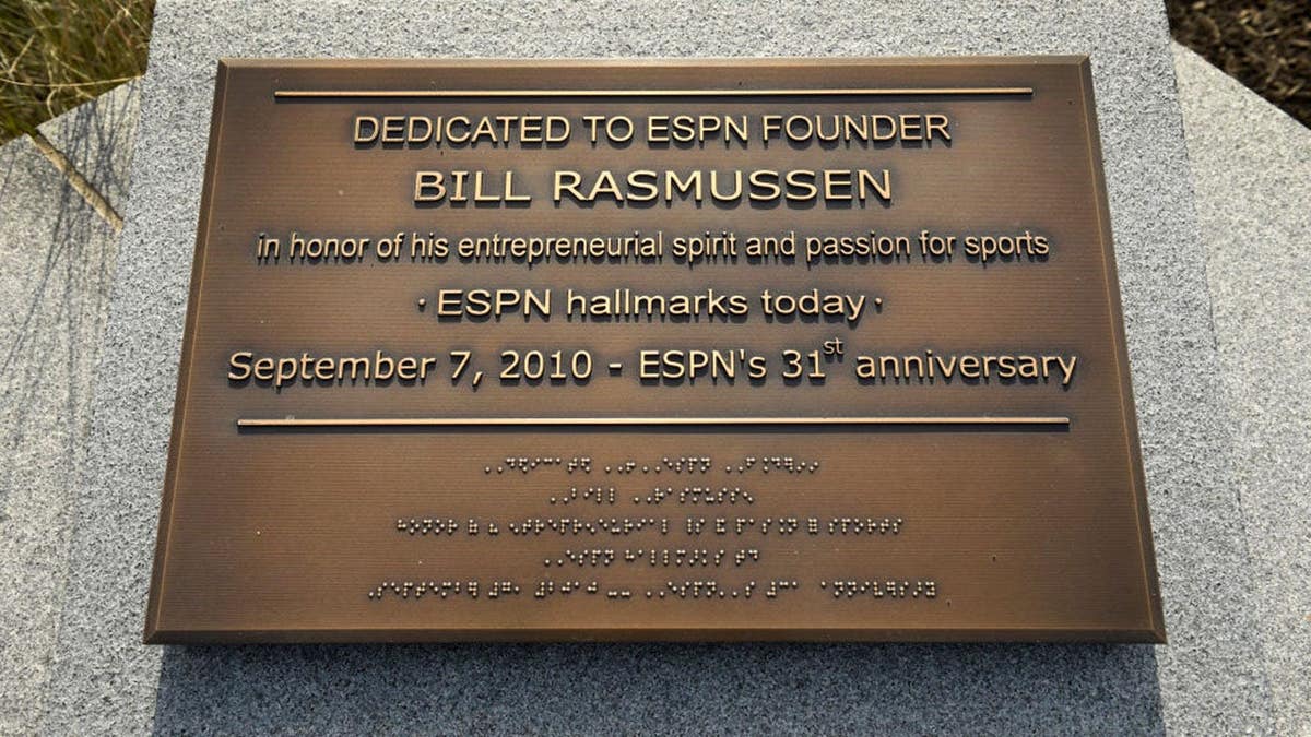 Bill Rasmussen stands beside a plaque dedicated to him as ESPN founder.
