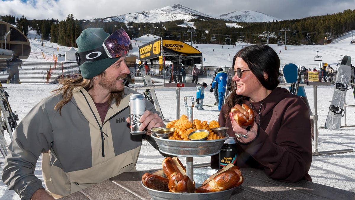 A pair of skiers enjoys a hot dog tower.