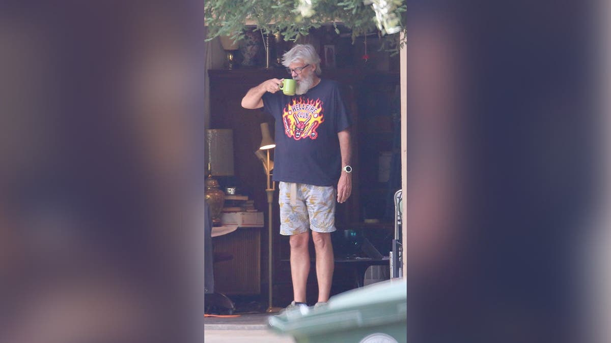 image shows Hooker standing and holding green coffee cup