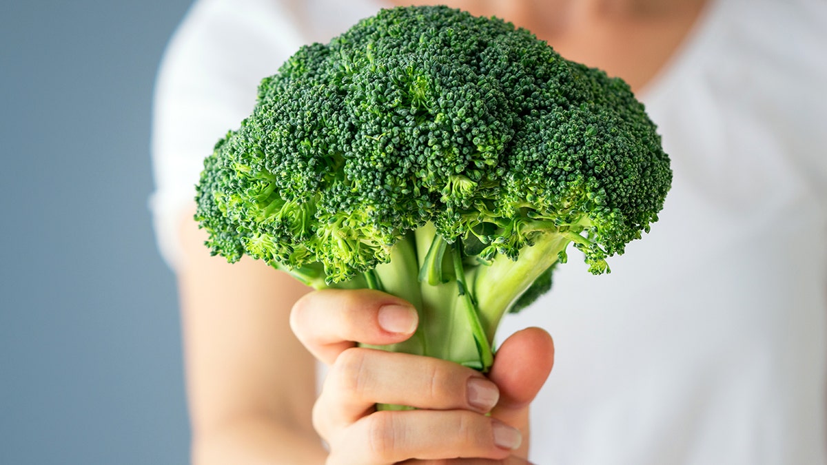 A woman's hand holds a head of raw broccoli.
