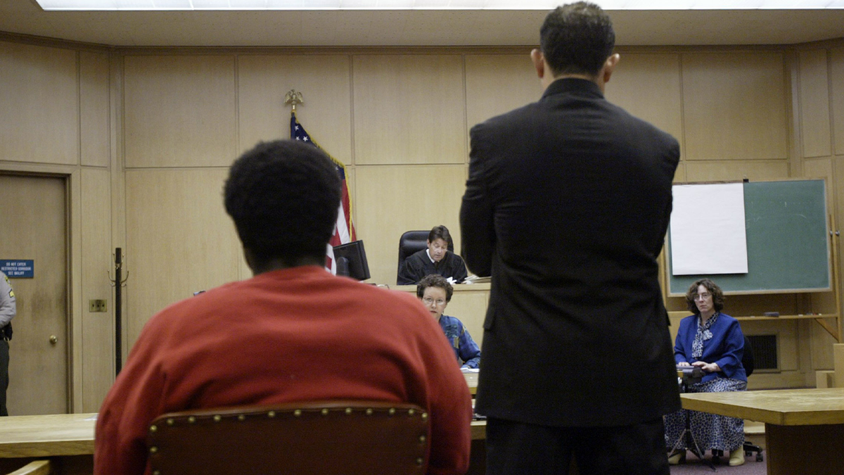 A man in an orange jail jumpsuit and his attorney shown from behind in a california courtroom during a hearing for David Hill, the man convicted of killing SF Police Officer Isaac Espinoza