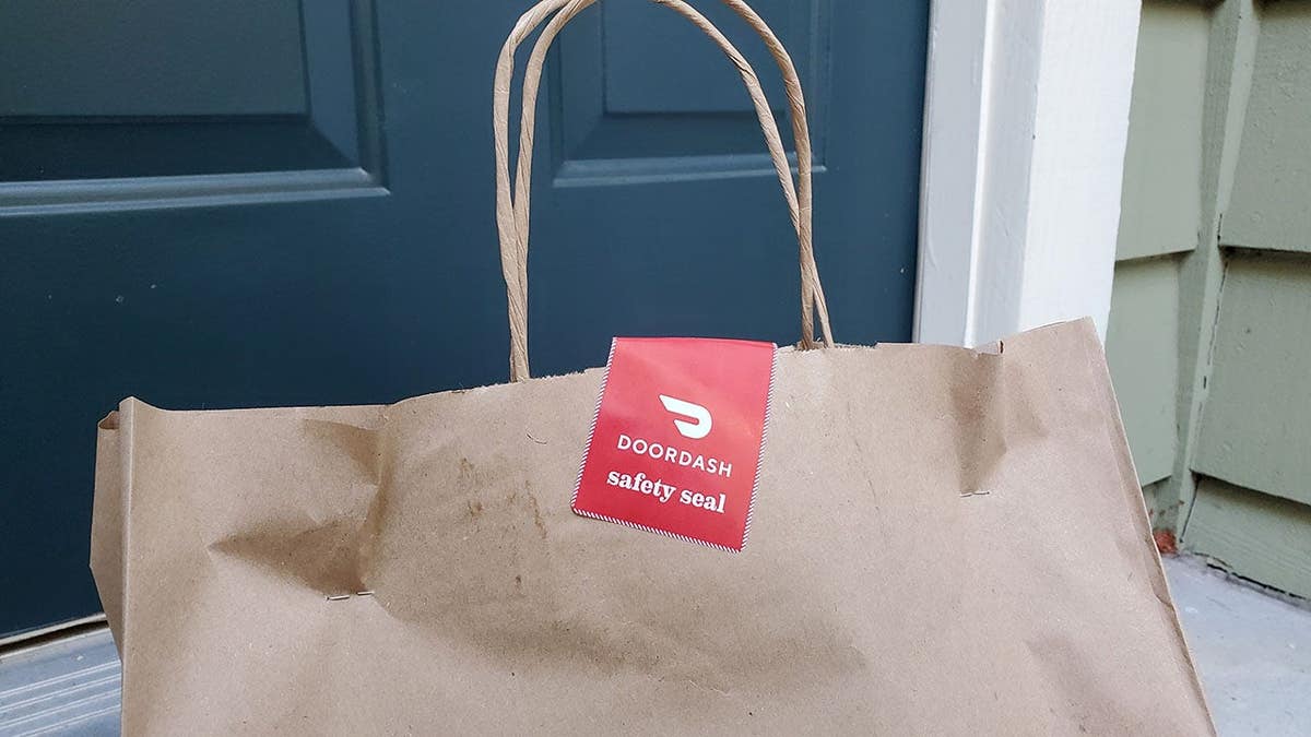 Brown paper bag with a DoorDash safety seal sticker sits near a front door.