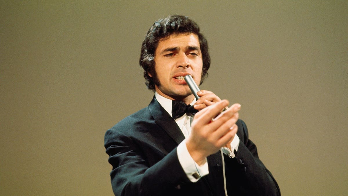 Engelbert Humperdinck sings into a microphone in close-up.