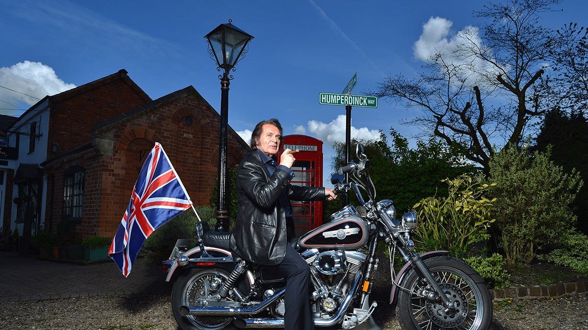 Englebert Humperdinck poses on a Harley Davidson motorcycle with a Union flag.