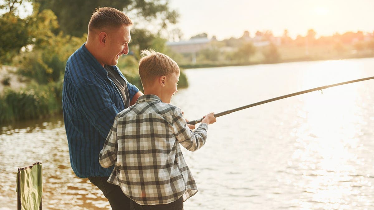 Father and son fishing together outdoors during summer.
