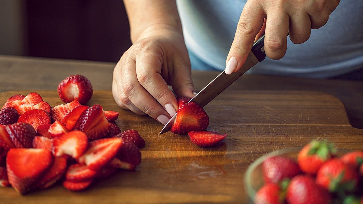 A woman slices a ripe strawberry on a cutting board.
