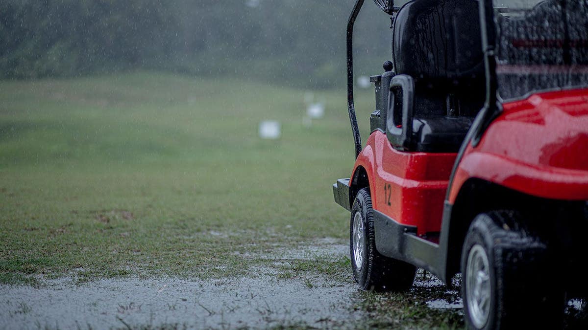 Golf cart sits on a wet field during rain.