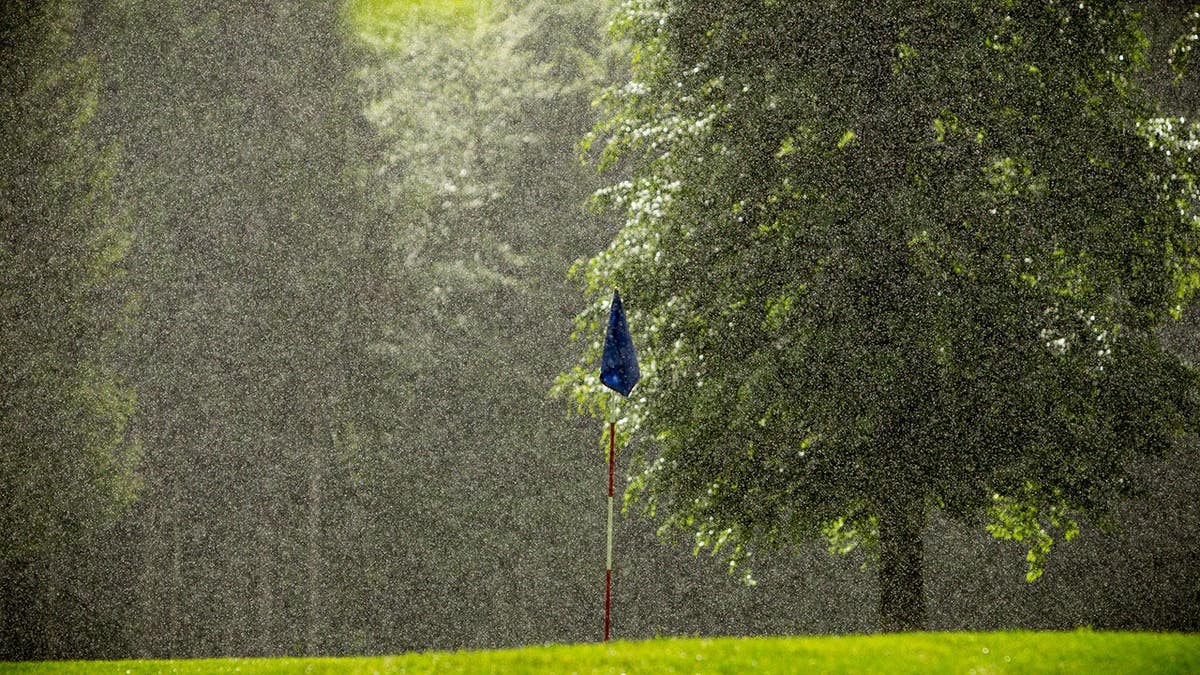 A golf flag stands in heavy rain on a golf course.