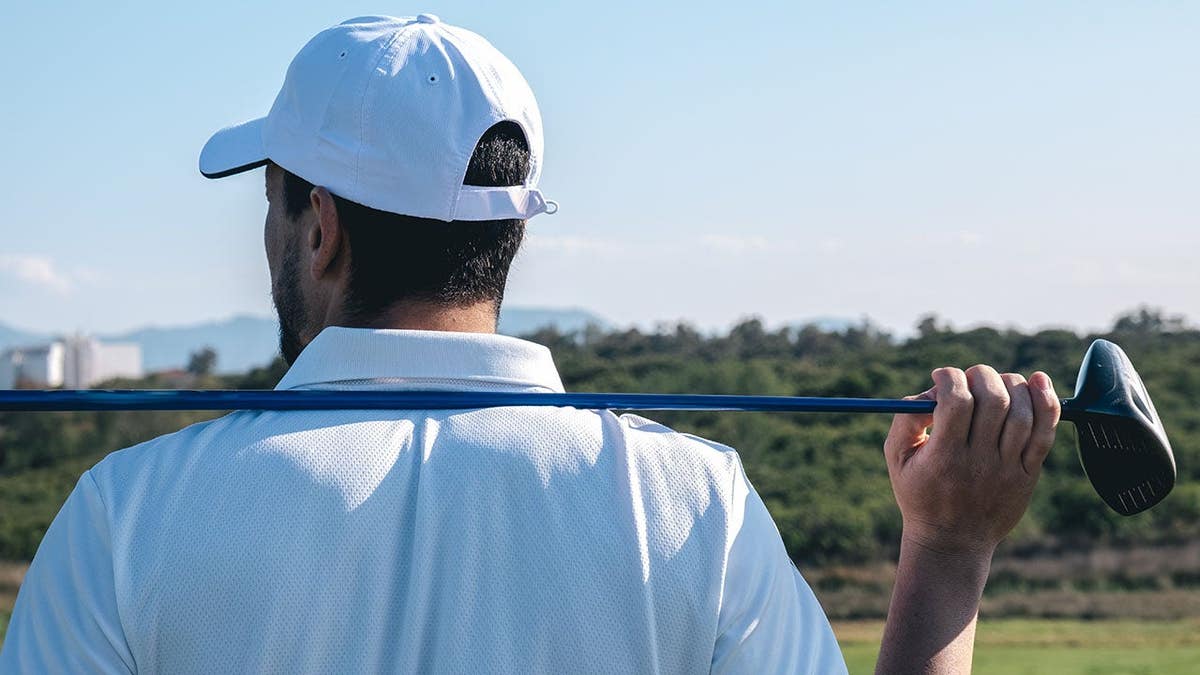 Golfer stands with golf club on shoulders overlooking a golf course.
