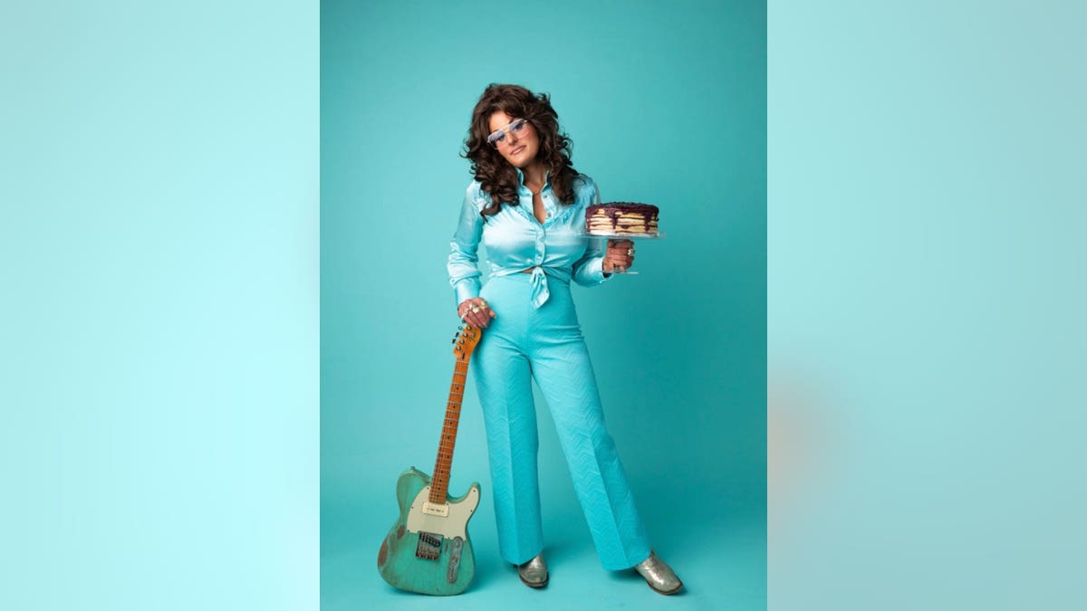 Hannah Dasher in aqua blue holding a guitar