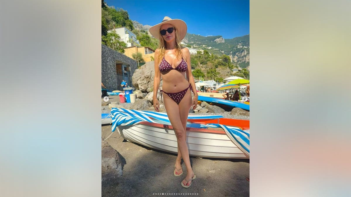 Heather Graham in a red and white polka dot bikini in front of a canoe.