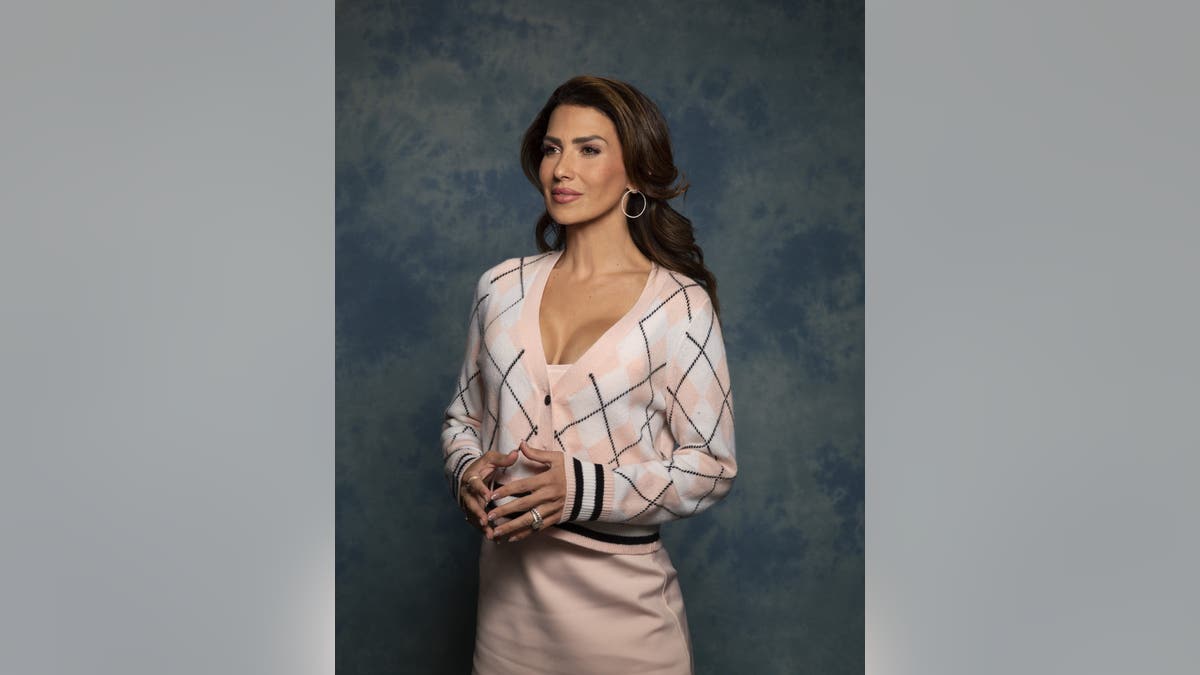 Hilaria Baldwin standing with her hands clasped in front of a studio backdrop.