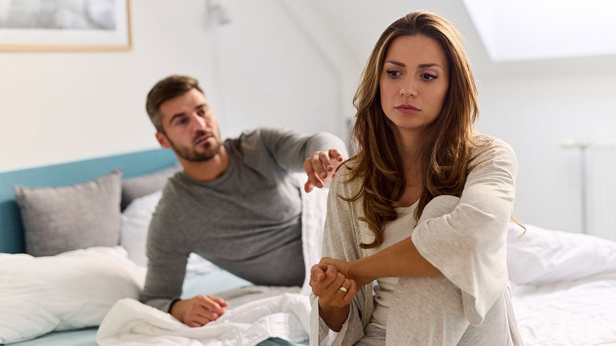 Couple sits on bed facing away from each other.