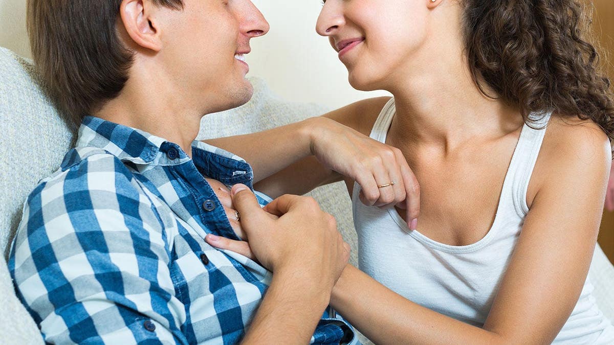 A man stands near a couch as a couple sits together.