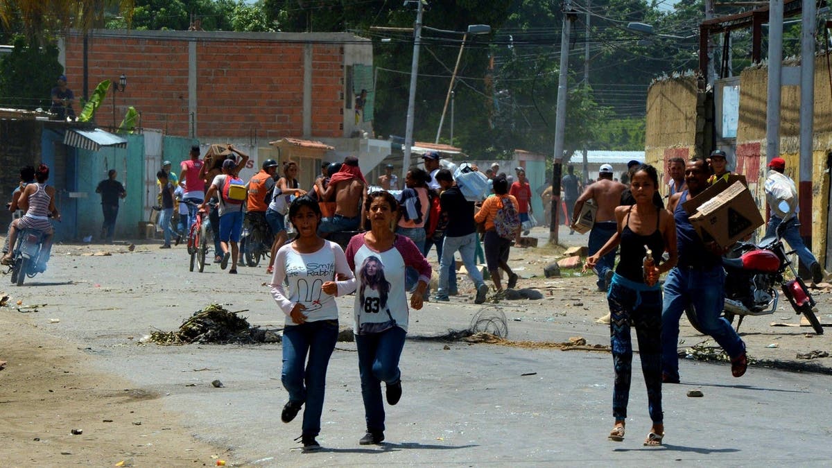 Locals run carrying stolen merchandise during looting in Maracay, Venezuela.