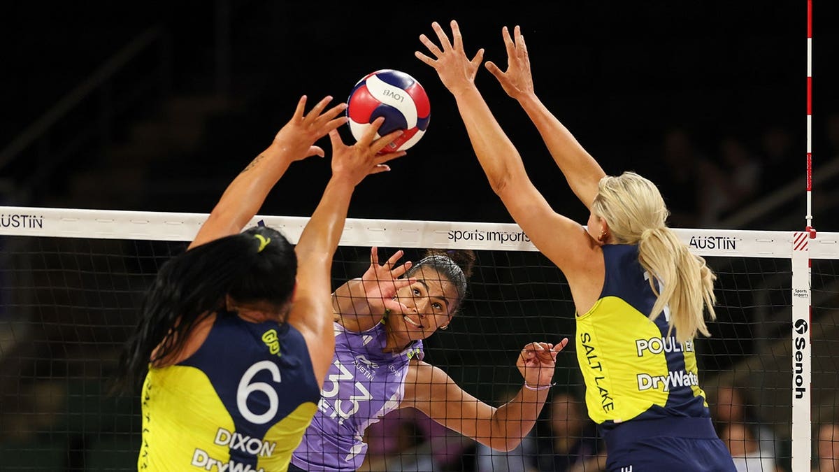 Logan Eggleston spikes the ball as Tori Dixon and Jordyn Poulter jump to block during a volleyball match.