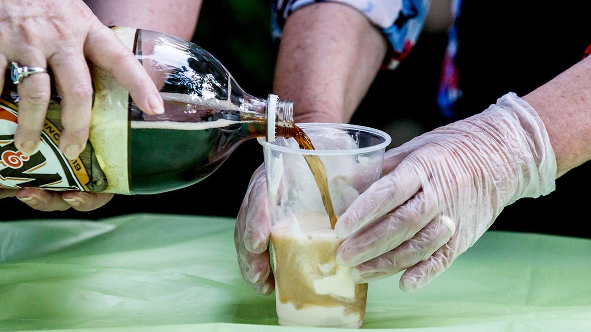 A&W Root Beer is poured into a clear plastic cup to make a root beer float.