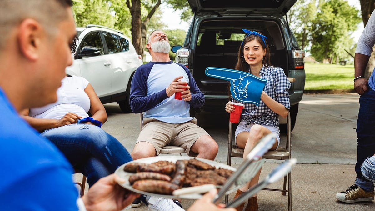 Man handing out burgers at a tailgate party.