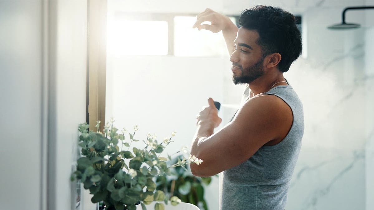 A man sprays deodorant under his arm.