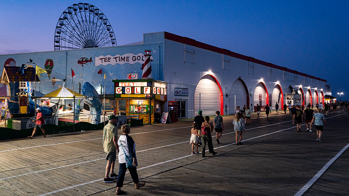 People walk along the Ocean City, New Jersey, boardwalk as the Ferris wheel rises in the background