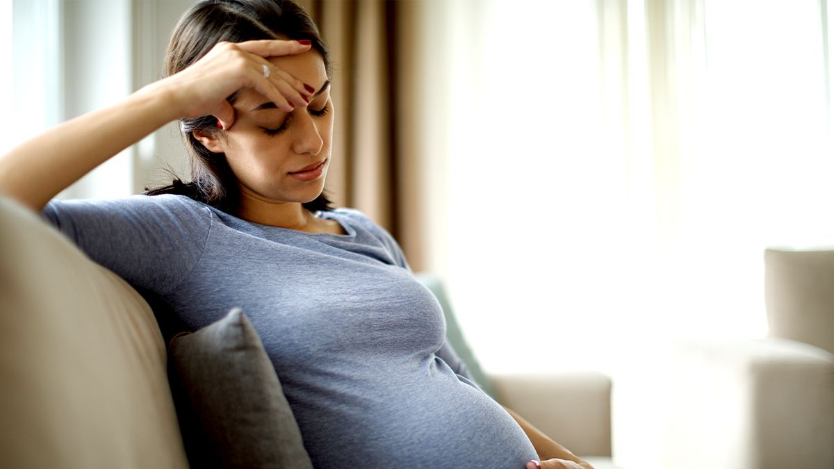 Pregnant woman holds her belly while sitting on a couch.