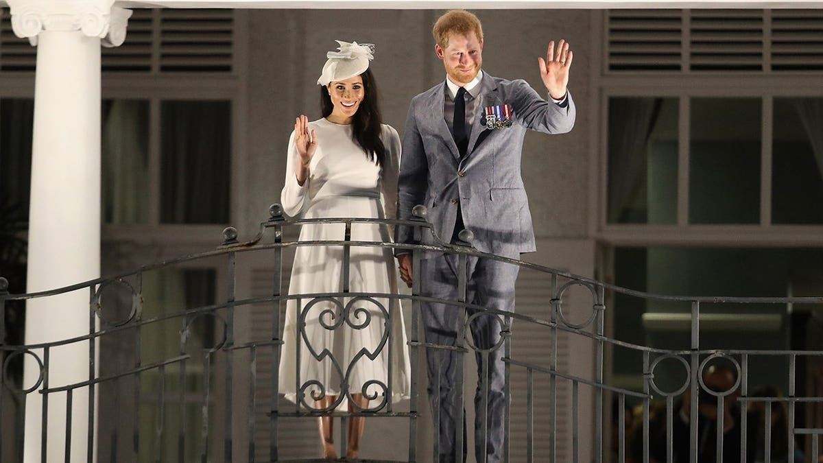 Prince Harry and Meghan, Duke and Duchess of Sussex, wave from a hotel balcony.