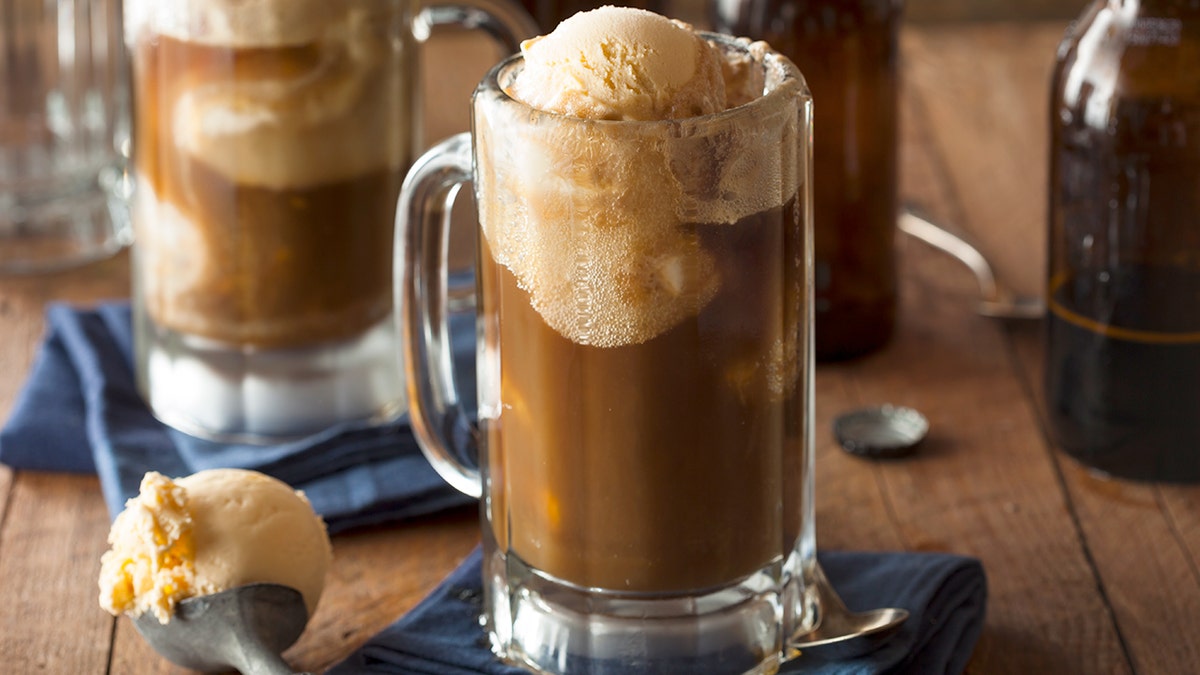 A root beer float in a glass mug next to a scoop of vanilla ice cream.