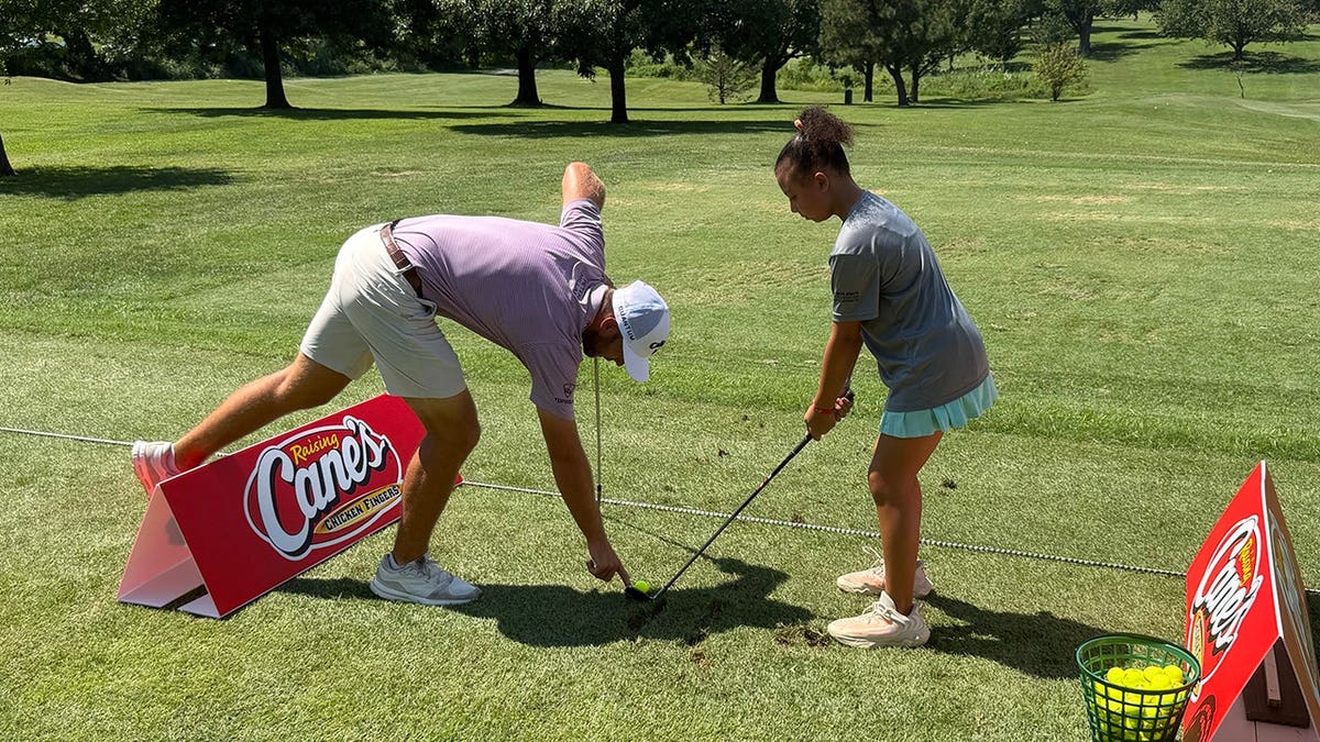 PGA Tour golfer Sam Burns helping a young golfer with her setup during a youth golf event in St. Louis.
