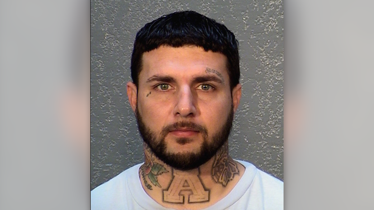 Santiago Rogers has short black hair, neck and face tattoos, and a short beard in this mugshot photo