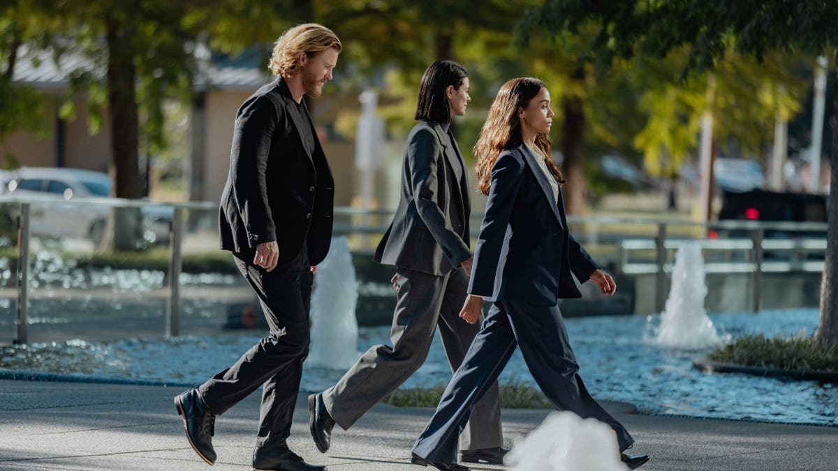 Thad Luckinbill, Laysla De Oliveira and Zoe Saldaña stand together in a scene from Lioness.