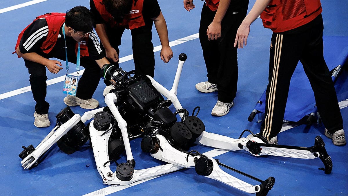 Maintenance team members check on Tiangong Ultra humanoid robots after they fall during a race.