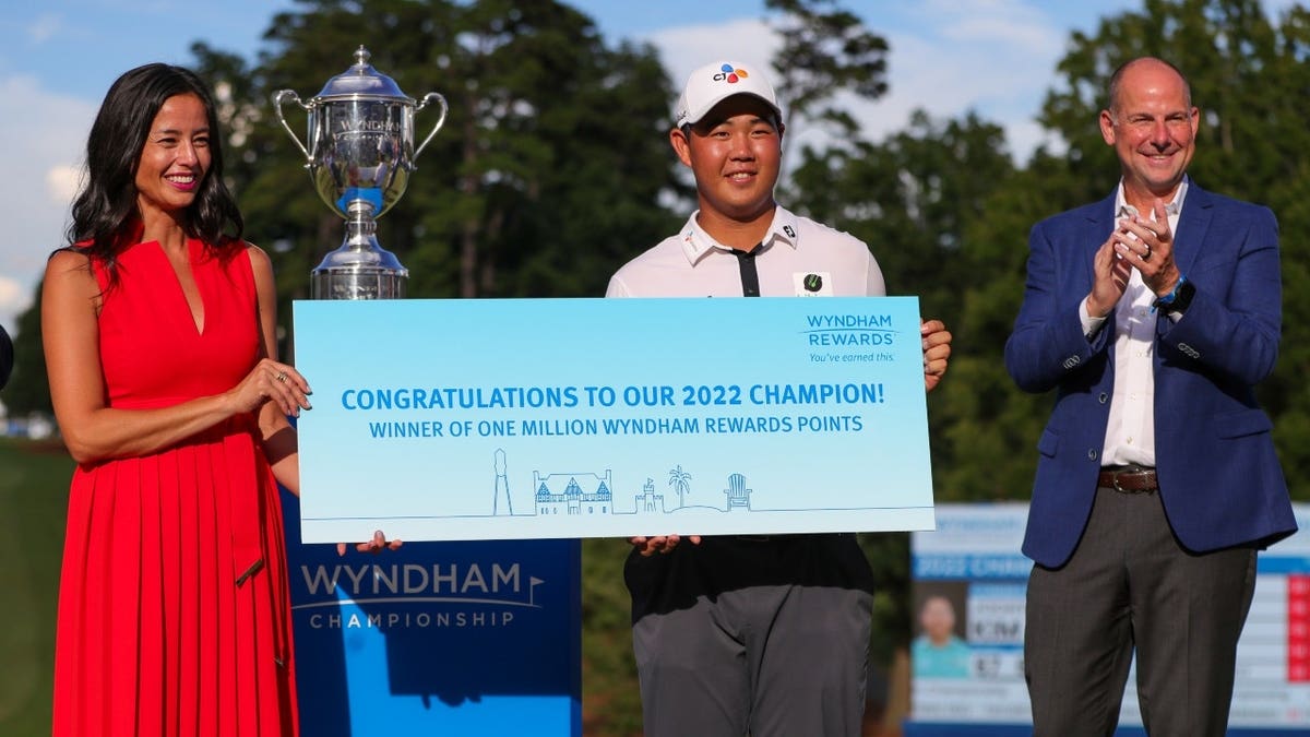Tom Kim is presented with one million Wyndham rewards points and a trophy after winning the 2022 Wyndham Championship at Sedgefield Country Club in Greensboro, North Carolina.