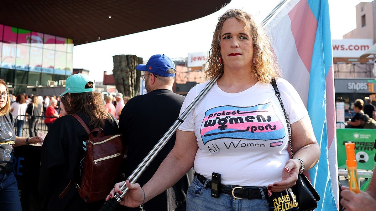 Trans athlete supporters hold signs and flags outside Barclays Center before a WNBA game.