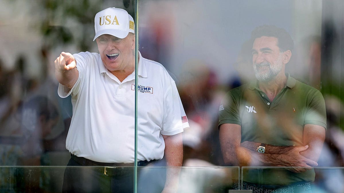 Donald Trump points while Yasir Al-Rumayyan looks on at a golf event.