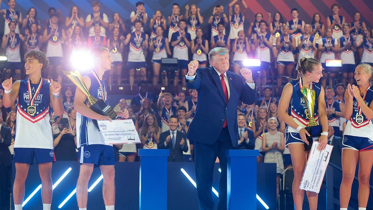 President Donald Trump gestures next to youth athletics competition winners as confetti falls.