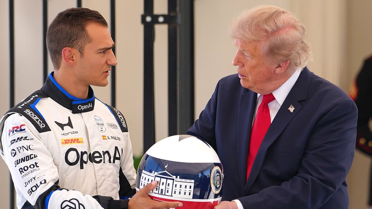 President Donald Trump receives a racing helmet from IndyCar champion Alex Palou as Roger Penske looks on.