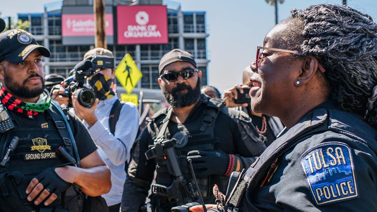 A Tulsa police officer stands between armed demonstrators during a Tulsa Race Massacre commemoration event.