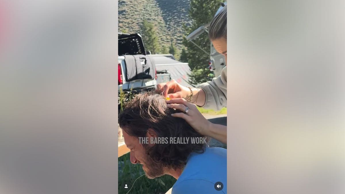 Tyler Hubbard sitting as his wife takes a fish hook out of his head.