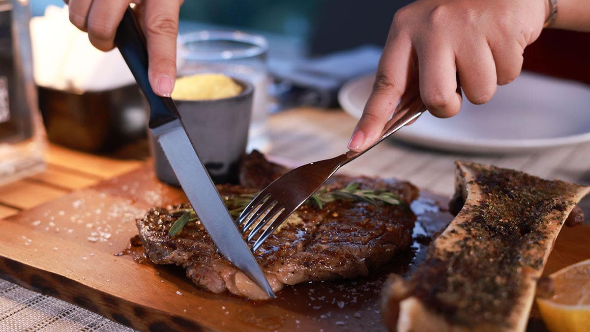 Woman cuts pork steak with knife and fork at a restaurant table.