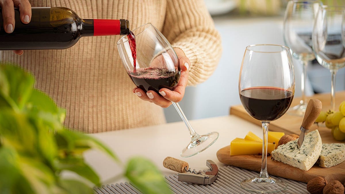 Woman pours red wine into a glass at a party table.