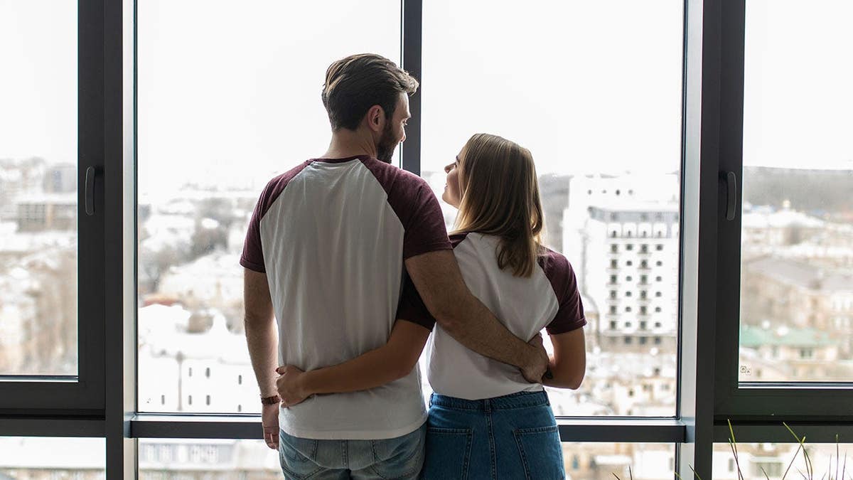 Young couple embracing near a window in a new apartment.