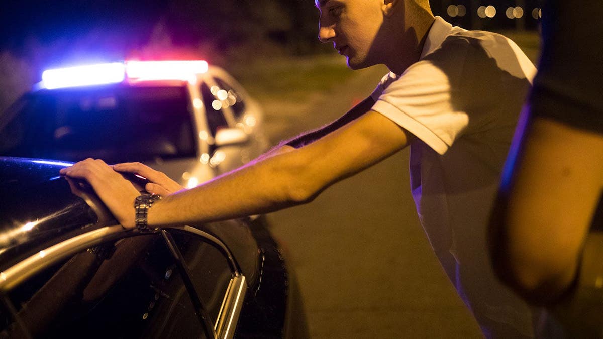 Young man sits in vehicle during police stop.
