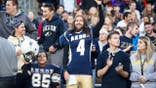 Akron Zips fans dressed in uniforms cheer in the stands during a college football game.