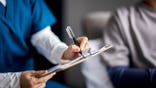 A doctor writes on a clipboard.