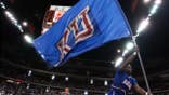 Kansas cheerleader waves school flag as team enters court before NCAA tournament game.