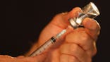 A syringe extracts liquid from a medical vial.