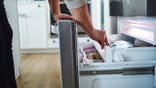 Man looks into an open freezer drawer of a refrigerator.