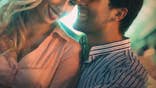 Man and woman sit at a bar holding drinks while flirting.