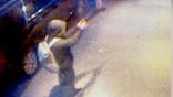 Man in dark hoodie aiming a gun and wearing a backpack on a new york city sidewalk